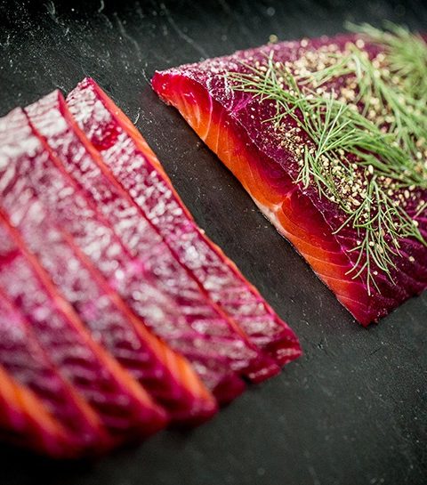 Sliced beetroot-cured salmon with fresh dill on a dark slate background, showcasing rich colours and textures