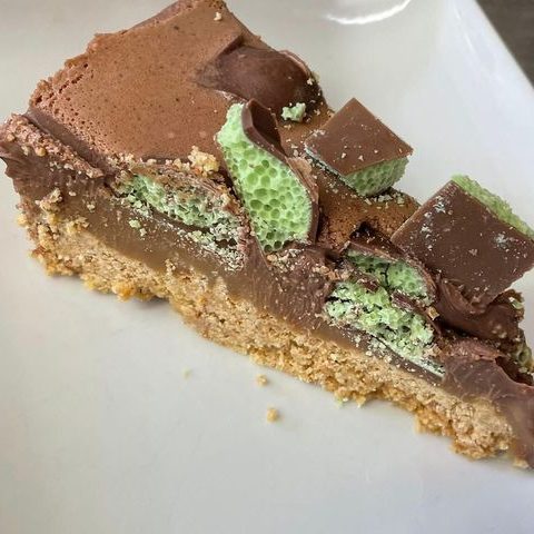 A slice of chocolate honeycomb cheesecake on a white plate, highlighting its creamy and crunchy texture