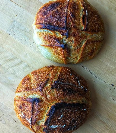 Two rustic sourdough loaves with golden crusts on a wooden table, showcasing artisanal baking skills