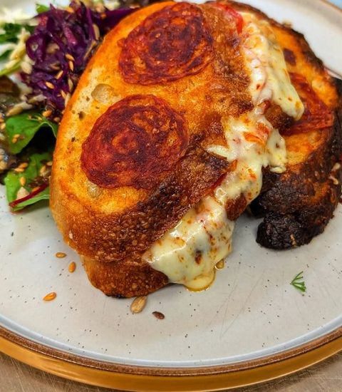 Grilled cheese sandwich with pepperoni and salad on a plate, featuring melted cheese and toasted bread