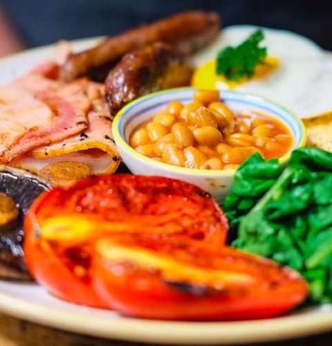 Full English breakfast with eggs, sausages, bacon, beans, tomatoes, mushrooms, and spinach on a plate