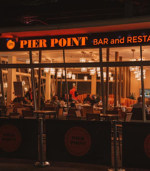 Pier Point Bar and Restaurant lit up at night with people dining inside, showing a warm and inviting atmosphere