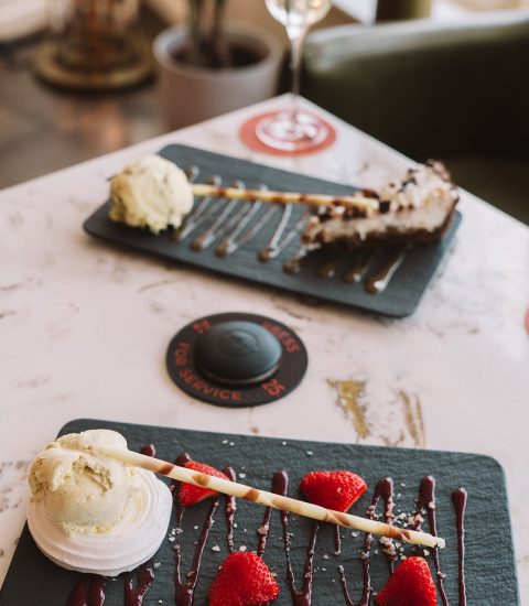 Dessert plate with strawberries, ice cream, and chocolate drizzle on a slate tray with champagne in the background