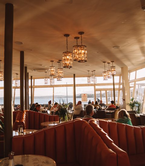 Sunny seaside restaurant with elegant lighting, plush seating, and panoramic ocean views, diners enjoying the ambiance