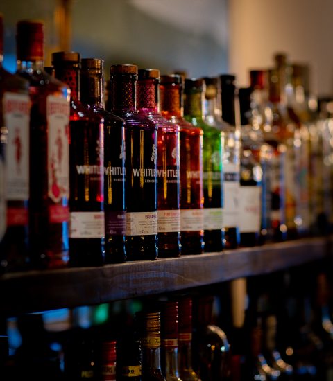 Assorted liquor bottles lined up on a wooden shelf in a dimly lit bar setting