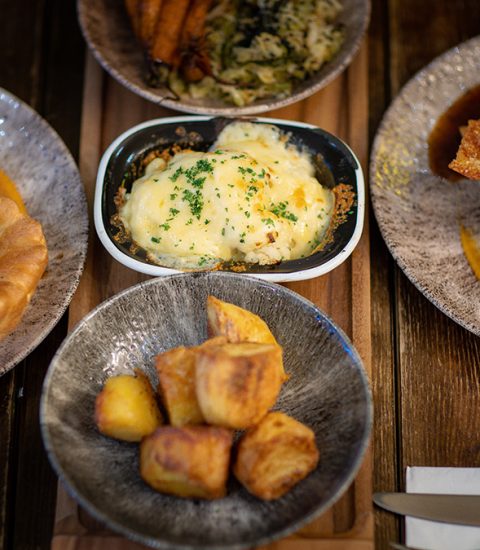 Traditional British Sunday roast with Yorkshire puddings, potatoes, and cheese-topped vegetables on a wooden table
