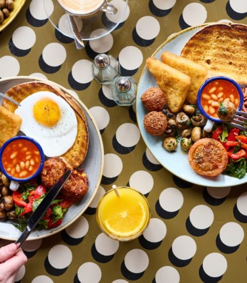Full English breakfast with fried eggs, mushrooms, baked beans, tomatoes, hash browns, and toast on a patterned table