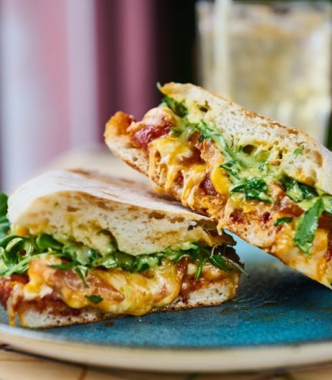 Gourmet sandwich with cheese, greens, and tomatoes on a blue plate, perfect for a delicious brunch meal