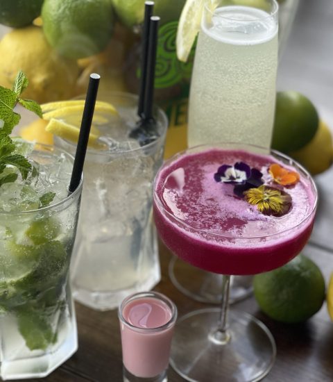 Refreshing mixed cocktails with lemon and mint garnish on a wooden table, surrounded by fresh lemons and limes
