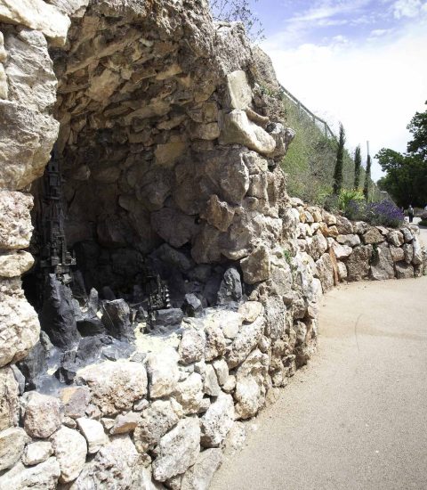 Stone grotto by a park pathway with trees and sky in the background
