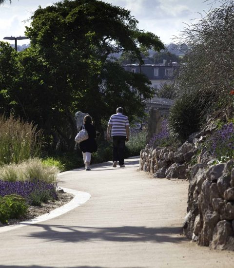 Couple walking on a scenic park pathway surrounded by greenery and rocks on a sunny day