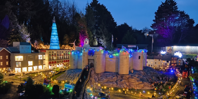 Model village illuminated at night with colourful lights, featuring a miniature castle and buildings surrounded by trees