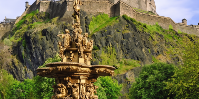 Golden fountain with ornate statues in front of Edinburgh Castle, surrounded by lush gardens in Edinburgh, Scotland