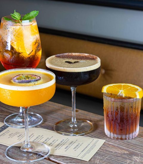 Assorted cocktails on a wooden table with a menu, garnished with fruit and mint leaves