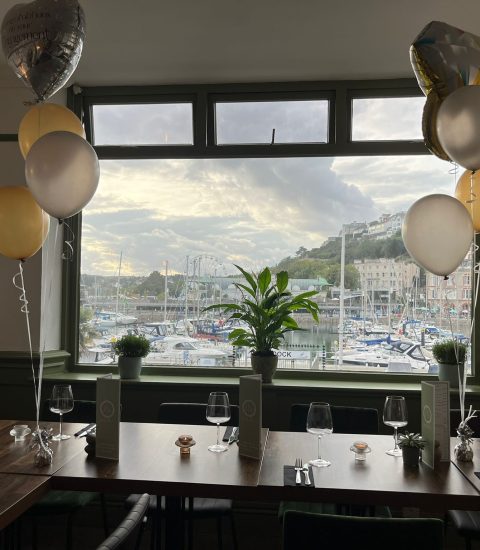 Restaurant table with balloons overlooking a marina, set for an engagement celebration near harbour in daylight