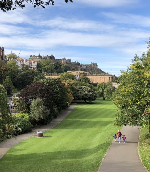 Family strolling through Princes Street Gardens in Edinburgh with a view of historic buildings and lush greenery