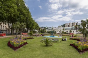 Beautiful public garden with colorful flowers, fountain, and people enjoying a sunny day under a blue sky