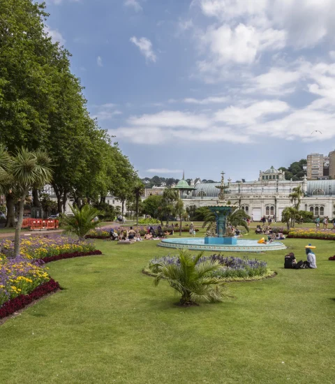 Beautiful public garden with colorful flowers, fountain, and people enjoying a sunny day under a blue sky