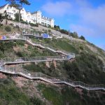 Scenic zigzag pathway on a hillside with white buildings and lush greenery under a blue sky