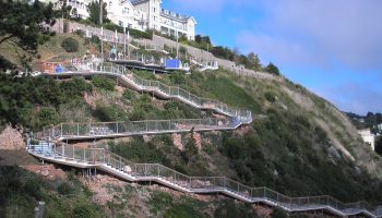 Scenic zigzag pathway on a hillside with white buildings and lush greenery under a blue sky