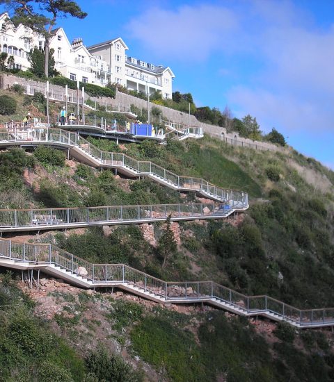 Scenic zigzag pathway on a hillside with white buildings and lush greenery under a blue sky