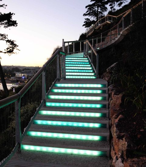 Glowing steps leading up a hill at twilight, overlooking a scenic view of a waterfront and distant lights