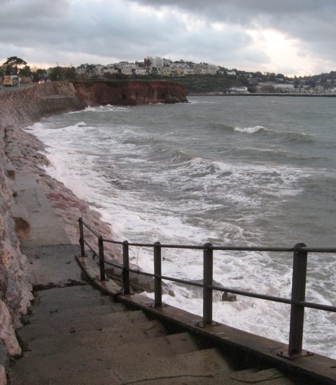 Coastal path with steps leading to the ocean in Torquay, UK, with waves crashing against the shoreline