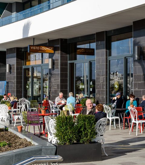 Outdoor seating area of Visto Lounge Café with people sitting and enjoying a sunny day on the promenade