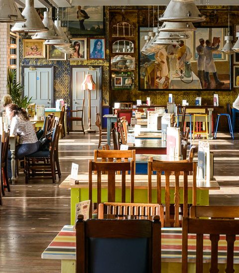 Cosy café with patrons enjoying coffee and conversation, vibrant decor and artwork on walls, natural light streaming in