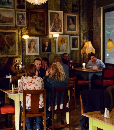 Cosy restaurant with diners enjoying meals and chatting, surrounded by art-filled walls and warm lighting