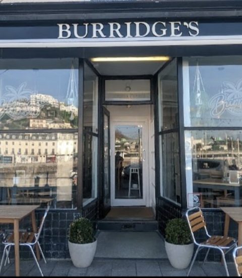Front view of Burridge's cafe with outdoor seating and harbour reflection in windows