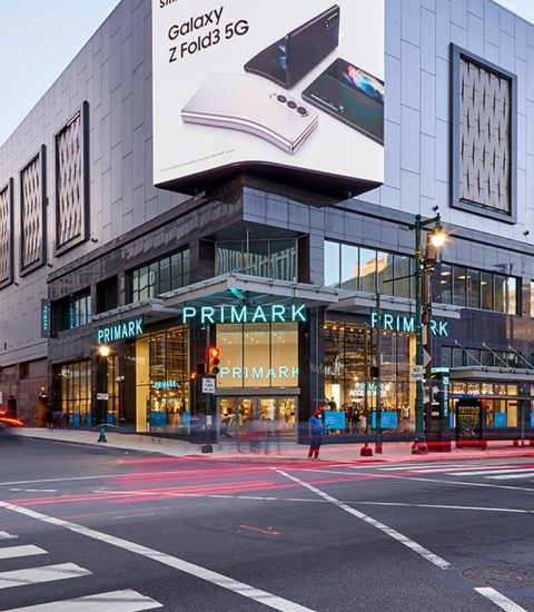 Primark store at a busy street intersection with a large Samsung Galaxy billboard above