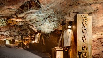 Underground display showcasing mining history with rustic wooden signs and dim lighting in a rocky cave setting
