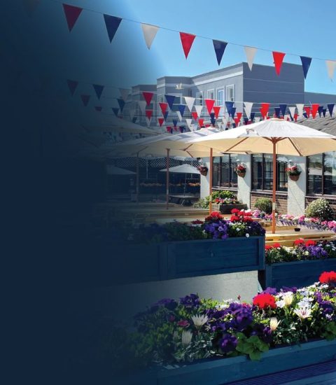 Colourful outdoor café with bunting and flowers under a clear blue sky in a vibrant garden setting