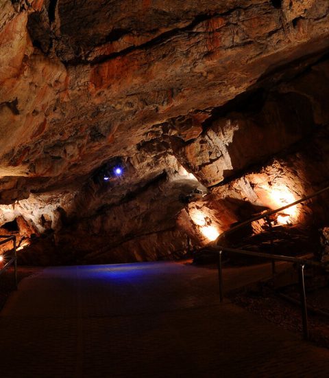 Illuminated underground cavern with rocky walls and pathway, showcasing natural geological formations