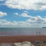 People enjoying a sunny day at the beach, with a view of the sea and fluffy clouds in the blue sky