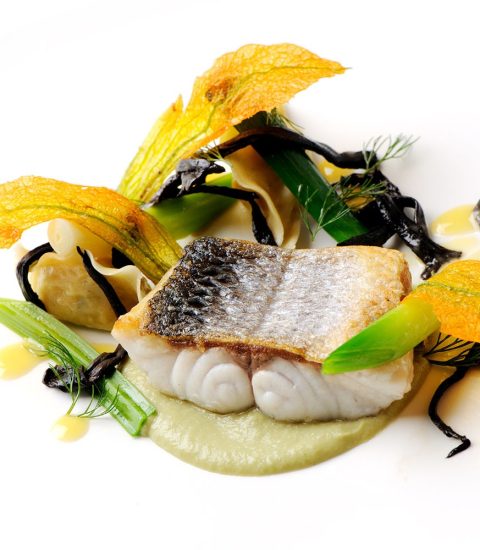 Gourmet dish with seared fish, green vegetables, and edible flowers on a white plate, artistic food presentation
