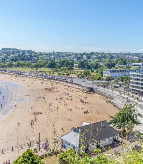 Beachfront with vibrant buildings and people enjoying a sunny day at the seaside in Torquay, UK