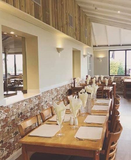 Cosy restaurant interior with wooden tables set for dining, featuring rustic brick walls and large windows with views