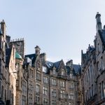 Historic stone buildings lining a street under a clear blue sky in Edinburgh, Scotland