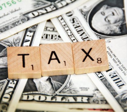 Wooden tiles spell TAX on top of various U.S. dollar bills, symbolising financial obligations